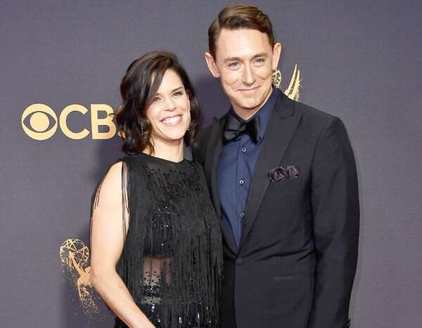 JJ Feild in a blue t-shirt and black coat posing with his wife in a black dress.